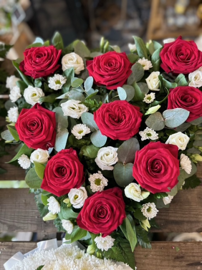 Crimson Heart Tribute - A striking heart-shaped funeral tribute arranged in rich red and soft white tones, beautifully finished with fresh greenery for a heartfelt farewell.