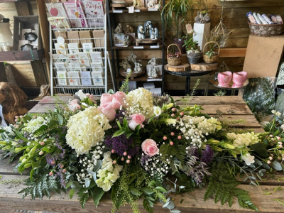 Pink & White Casket Spray - An elegant casket spray arranged in soft pink, white and subtle purple tones, complemented by lush greenery for a beautiful and heartfelt farewell.