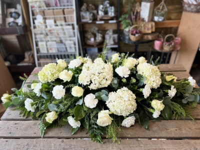 White Casket Spray - A timeless casket spray arranged in elegant white and cream tones, complemented by lush greenery for a graceful and heartfelt tribute.