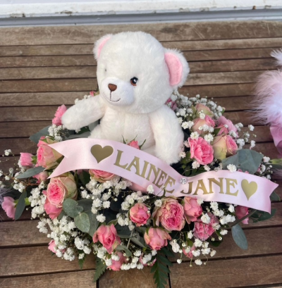 Personalised Teddy Wreath - A beautiful funeral wreath featuring a keepsake teddy bear and personalised name banner, surrounded by delicate flowers and foliage.