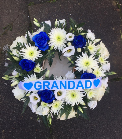 Blue Tribute Wreath - A classic funeral wreath of crisp white blooms and striking blue roses, finished with a personalised tribute ribbon.