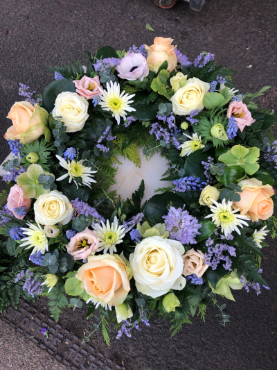 Serenity Wreath - A graceful funeral wreath featuring soft peach, cream and lilac blooms, beautifully complemented by lush greenery.