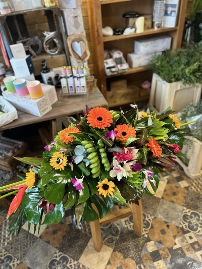 Tropical Paradise Spray - A bold funeral spray bursting with vibrant orange, yellow and pink blooms, complemented by lush tropical foliage.