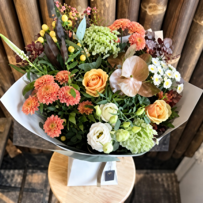Copper Charm - A stylish bouquet of warm orange, peach and soft green blooms, beautifully complemented by rich seasonal foliage.