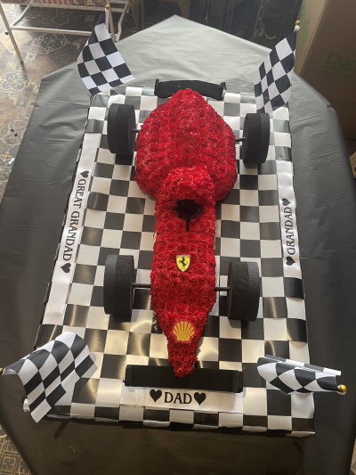 Ferrari Funeral Tribute - F1 Car designed by our senior florist, scaled to look realistic, but maintain that floral charm. The flags add the finishing touches.
